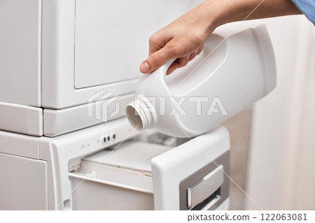 female hand pouring liquid laundry detergent from bottle into washing machine, closeup female hand pouring liquid laundry detergent from bottle into washing machine, closeup 122063081