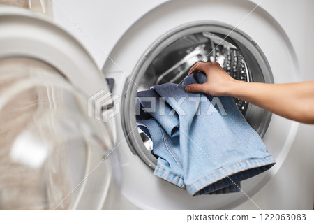 female hand putting jeans into the washing machine, close-up 122063083