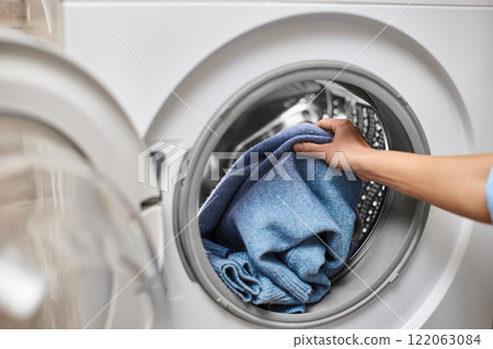 Woman putting blue wool clothes into the washing machine, close-up 122063084