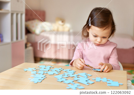 Cute little child girl connecting puzzle pieces on wooden desk in room 122063092