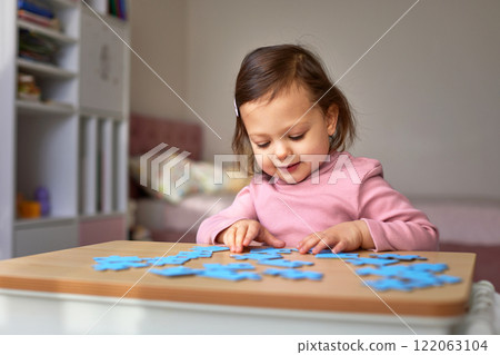 Cute little child girl doing puzzle on wooden table, baby learns to solve problems Cute little child girl doing puzzle on wooden table, baby learns to solve problems 122063104