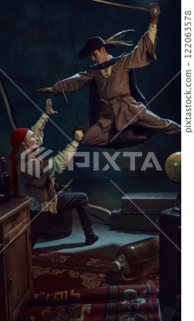 Two med, dressed like antique pirates, in bandana and hat, fighting dynamically with swords against dark vintage background with retro carpet, furniture and suitcase Two med, dressed like antique pirates, in bandana and hat, fighting dynamically with swords against dark vintage background with retro carpet, furniture and suitcase 122063578