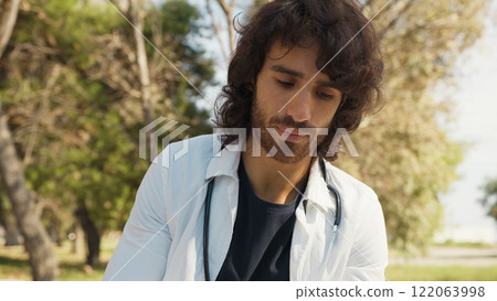 Male Doctor Writes Patient's Medical Record Outside In Hospital Park Among Trees Male Doctor Writes Patient's Medical Record Outside In Hospital Park Among Trees 122063998