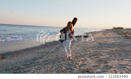 Girl Walks And Plays The Bass Instrument On The Beach Near The Ocean At Sunset 122063999