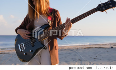 Girl Plays Bass Music Instrument On The Beach At Sunset Near Ocean 122064018