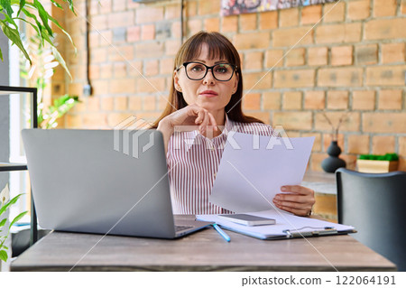 Middle-aged business woman working remotely with laptop in coworking Middle-aged business woman working remotely with laptop in coworking 122064191