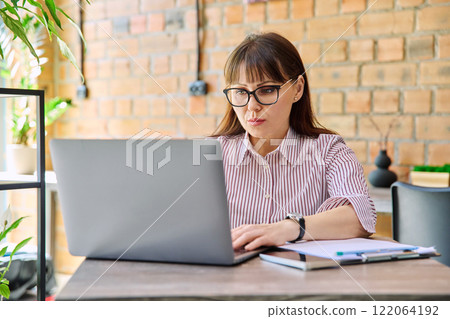 Middle-aged business woman working remotely with laptop in coworking Middle-aged business woman working remotely with laptop in coworking 122064192