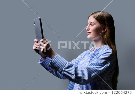 Teenage female student using digital tablet on gray studio background, profile view Teenage female student using digital tablet on gray studio background, profile view 122064273