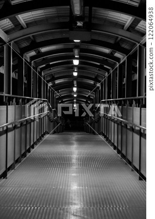 Pedestrian bridge with a metallic walkway and arched overhead structure at night Pedestrian bridge with a metallic walkway and arched overhead structure at night 122064938