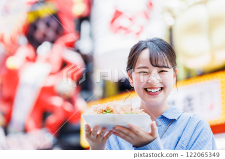 A woman eating the famous takoyaki in Dotonbori, Osaka 122065349