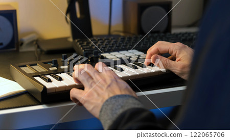 Close-up of a man composing a new music track using a MIDI keyboard controller in his cozy home studio, showcasing a creative and inspiring atmosphere Close-up of a man composing a new music track using a MIDI keyboard controller in his cozy home studio, showcasing a creative and inspiring atmosphere 122065706