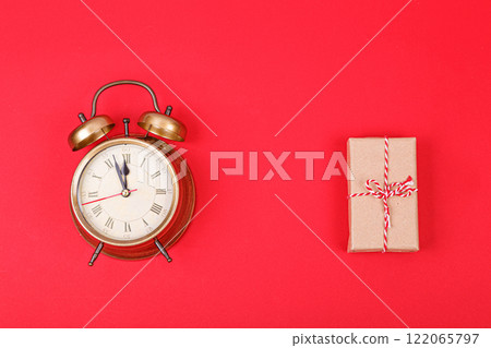New Year's clock in gold color with a gift on a red background 122065797