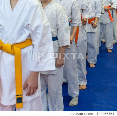 A close-up of a row of young athletes in white karate kimonos with clenched fists. 122066163