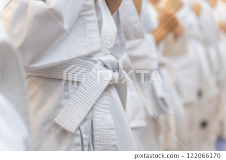A close-up of a row of young athletes in white karate kimonos with clenched fists. A close-up of a row of young athletes in white karate kimonos with clenched fists. 122066170