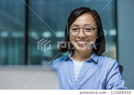 Asian Office worker with headset phone close up, woman working with laptop for video call, consulting customer customers sitting inside office at workplace. 122066438