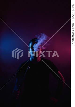 Silhouette of a man wearing glasses enjoying a serene moment surrounded by flickering smoke in a bright neon light in a hookah bar Silhouette of a man wearing glasses enjoying a serene moment surrounded by flickering smoke in a bright neon light in a hookah bar 122066492