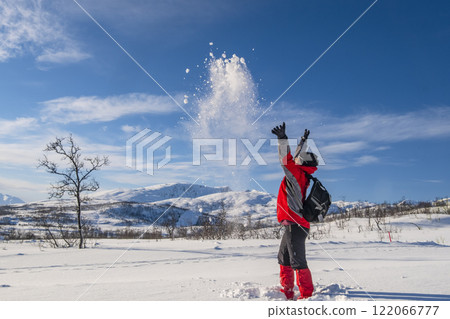 Sporty person in red sport jacket enjoys snow and breathtaking Norwegian landscape. Sunny winter activity. 122066777