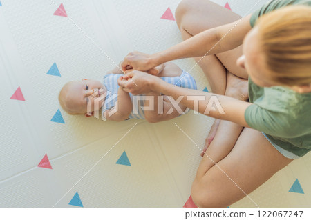 A mother practices baby gymnastics with her 3-month-old on a soft children's play mat. A joyful and nurturing moment focused on bonding, development, and care. Early childhood, fitness, and parenting A mother practices baby gymnastics with her 3-month-old on a soft children's play mat. A joyful and nurturing moment focused on bonding, development, and care. Early childhood, fitness, and parenting 122067247