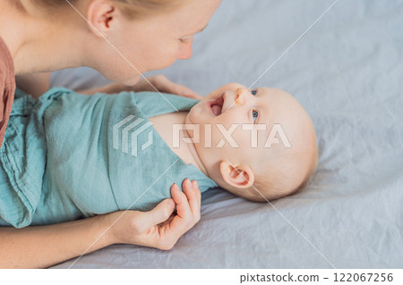 A mother gently wraps her baby in a soft muslin swaddle, providing warmth and comfort. A tender moment of care and love between mother and child. Motherhood, baby care, and nurturing concept 122067256