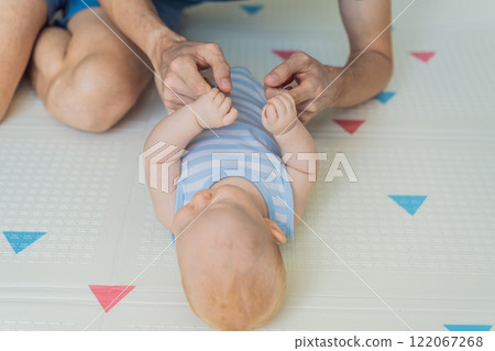 A baby lies on a soft children play mat while their father hands gently support and protect them. Heartwarming moment of care and connection. Parenthood, safety, and love concept A baby lies on a soft children play mat while their father hands gently support and protect them. Heartwarming moment of care and connection. Parenthood, safety, and love concept 122067268