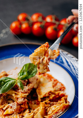 Close-up of a forkful of lasagna with fresh basil and tomato sauce, perfect for food photography Close-up of a forkful of lasagna with fresh basil and tomato sauce, perfect for food photography 122067694