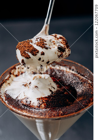 Indulgent creamy dessert spooned from a martini glass, dusted with rich cocoa powder 122067709