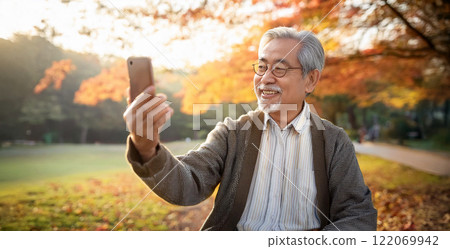 A senior man making a video call on his smartphone in the park. A senior man making a video call on his smartphone in the park. 122069942