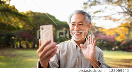 A senior man making a video call on his smartphone in the park. A senior man making a video call on his smartphone in the park. 122069943