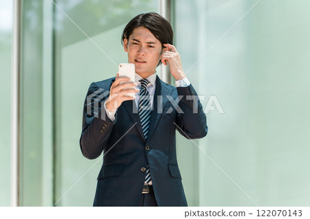 一位身穿西裝的年輕亞洲男性商人操作智慧型手機（打電話、擔心、找藉口、思考、遇到麻煩） 122070143