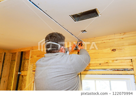 Contractor is cutting drywall on ceiling, installing drywall while wearing safety gear during home renovation project. 122070994