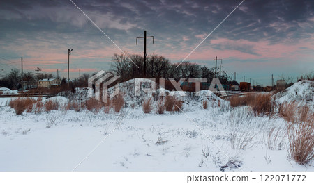 Snow blankets ground as leafless trees stand amidst quiet, deserted landscape under moody sky near railway tracks area 122071772