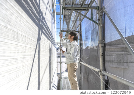 A man checking the progress of repair work on the exterior walls of a detached house A man checking the progress of repair work on the exterior walls of a detached house 122072949