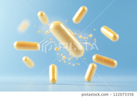 Yellow capsule disintegrating and releasing granules on light blue background 122073356