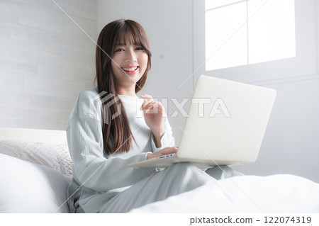 A woman using a computer on the bed. Image of lifestyle, freelance, working style and busy work A woman using a computer on the bed. Image of lifestyle, freelance, working style and busy work 122074319