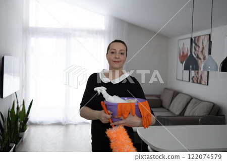 A woman confidently holds cleaning supplies in a stylish home, reflecting wellness and organization 122074579
