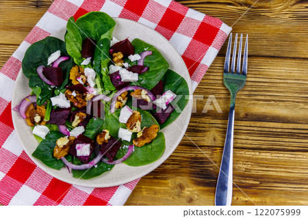 Tasty spinach salad with boiled beetroot, feta cheese, walnut and red onion on wooden table. Top view. Healthy vegetarian food 122075999