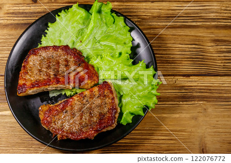 Grilled pork steaks with lettuce leaves on wooden table. Top view 122076772
