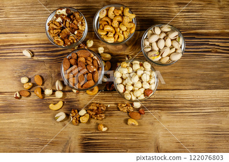 Assortment of nuts on wooden table. Almond, hazelnut, pistachio, walnut and cashew in glass bowls. Top view. Healthy eating concept 122076803