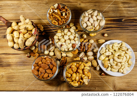 Assortment of nuts on wooden table. Almond, hazelnut, pistachio, peanut, walnut and cashew in small bowls. Top view. Healthy eating concept Assortment of nuts on wooden table. Almond, hazelnut, pistachio, peanut, walnut and cashew in small bowls. Top view. Healthy eating concept 122076804