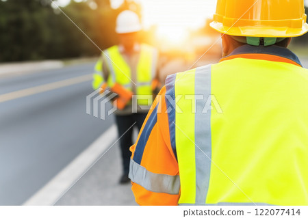 Safety-focused Construction Workers in Vests Collaborating on a Project at Sunrise 122077414