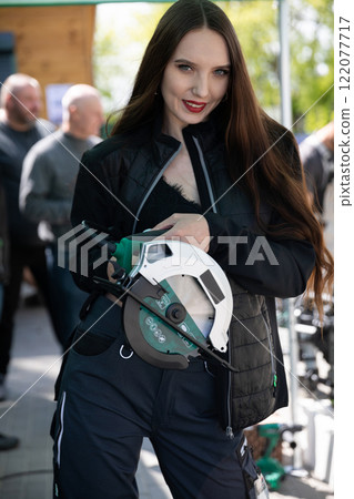 A highly skilled woman proudly holding a power tool while participating in an outdoor event A highly skilled woman proudly holding a power tool while participating in an outdoor event 122077717