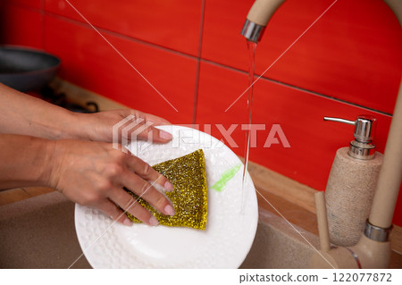 Washing dirty dishes at the kitchen sink using a sponge to scrub and clean them thoroughly 122077872