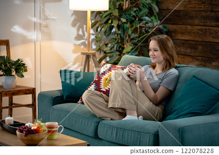 A Relaxing and Comfortable Evening at Home with a Young Woman Sitting on a Couch 122078228