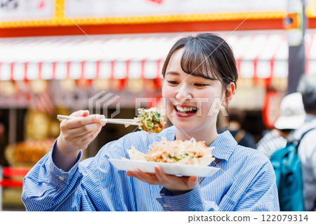 A woman eating the famous takoyaki in Dotonbori, Osaka A woman eating the famous takoyaki in Dotonbori, Osaka 122079314