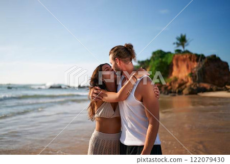 Affectionate couple embraces on sandy beach, serene sea. Man, woman share kiss, peaceful coastal scene. Intimate moment, couple enjoy romantic getaway. Love relationship, tranquility at seaside. 122079430