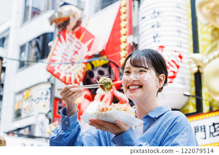 A woman eating the famous takoyaki in Dotonbori, Osaka 122079514