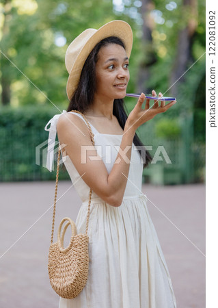 African American woman in white dress records audio message on smartphone. adorable female model 122081092
