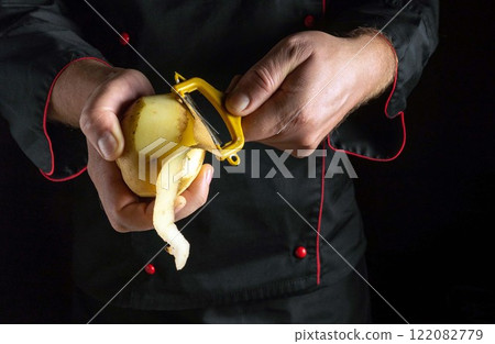 In a dramatic kitchen setting, a chef focuses intently as he skillfully peels a potato. Concept of cooking vegetable dish In a dramatic kitchen setting, a chef focuses intently as he skillfully peels a potato. Concept of cooking vegetable dish 122082779