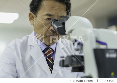 A middle-aged doctor in a white coat, excluding a microscope. Photo courtesy of Tokyo Electronics College, Denpa Gakuen Corporation. 122083390