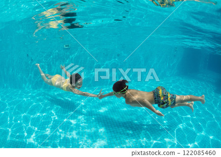 Happy kids have fun in swimming pool. Funny child swim, dive in pool - jump deep down underwater from poolside. Healthy lifestyle, people water sport activity, swimming lessons on holidays 122085460